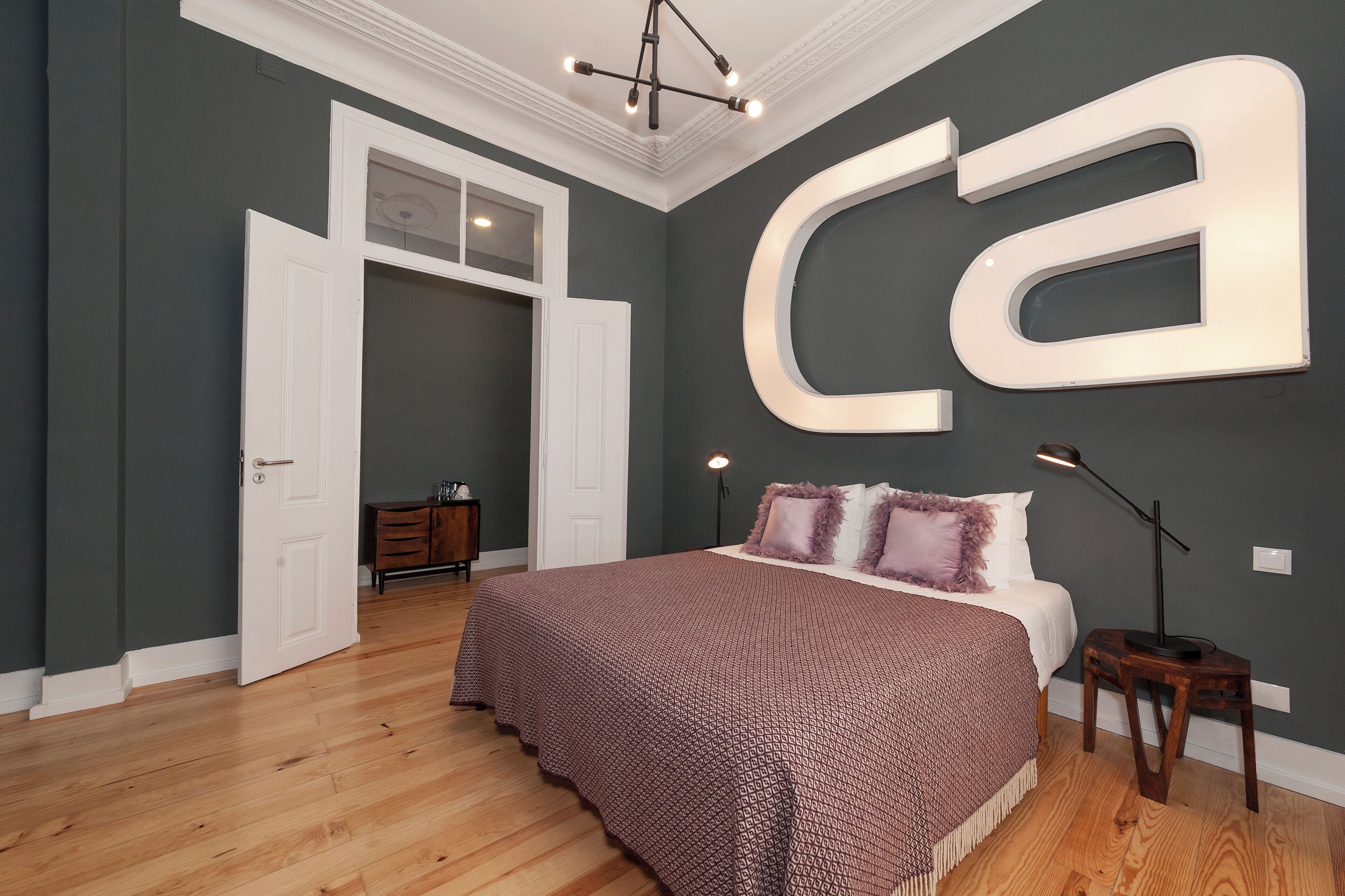 A bedroom with a large 'ca' sign on the wall, a bed with a patterned blanket, a nightstand, and a dresser.