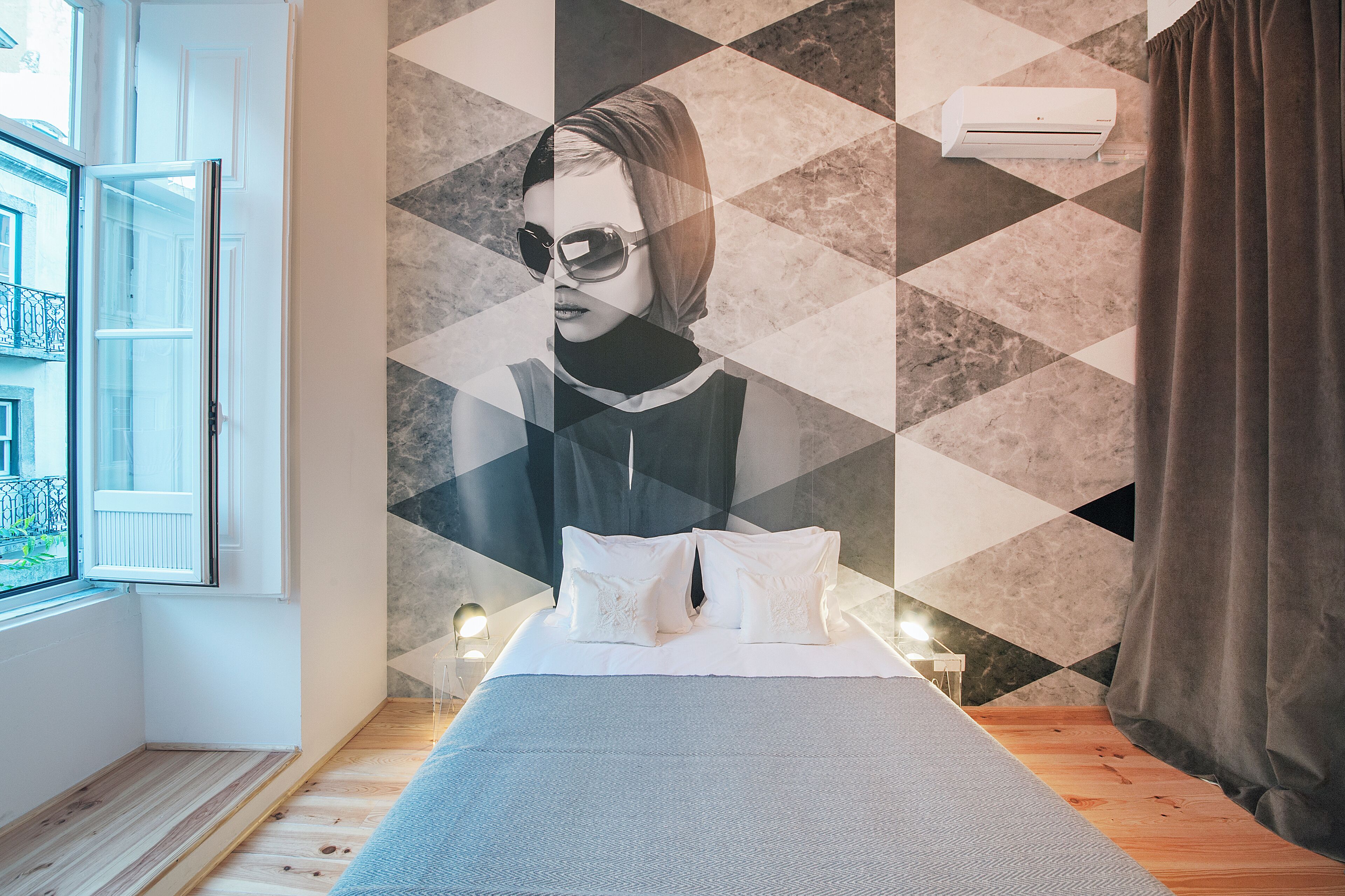 Een slaapkamer met een bed, kussens, een raam en een wandairconditioner.