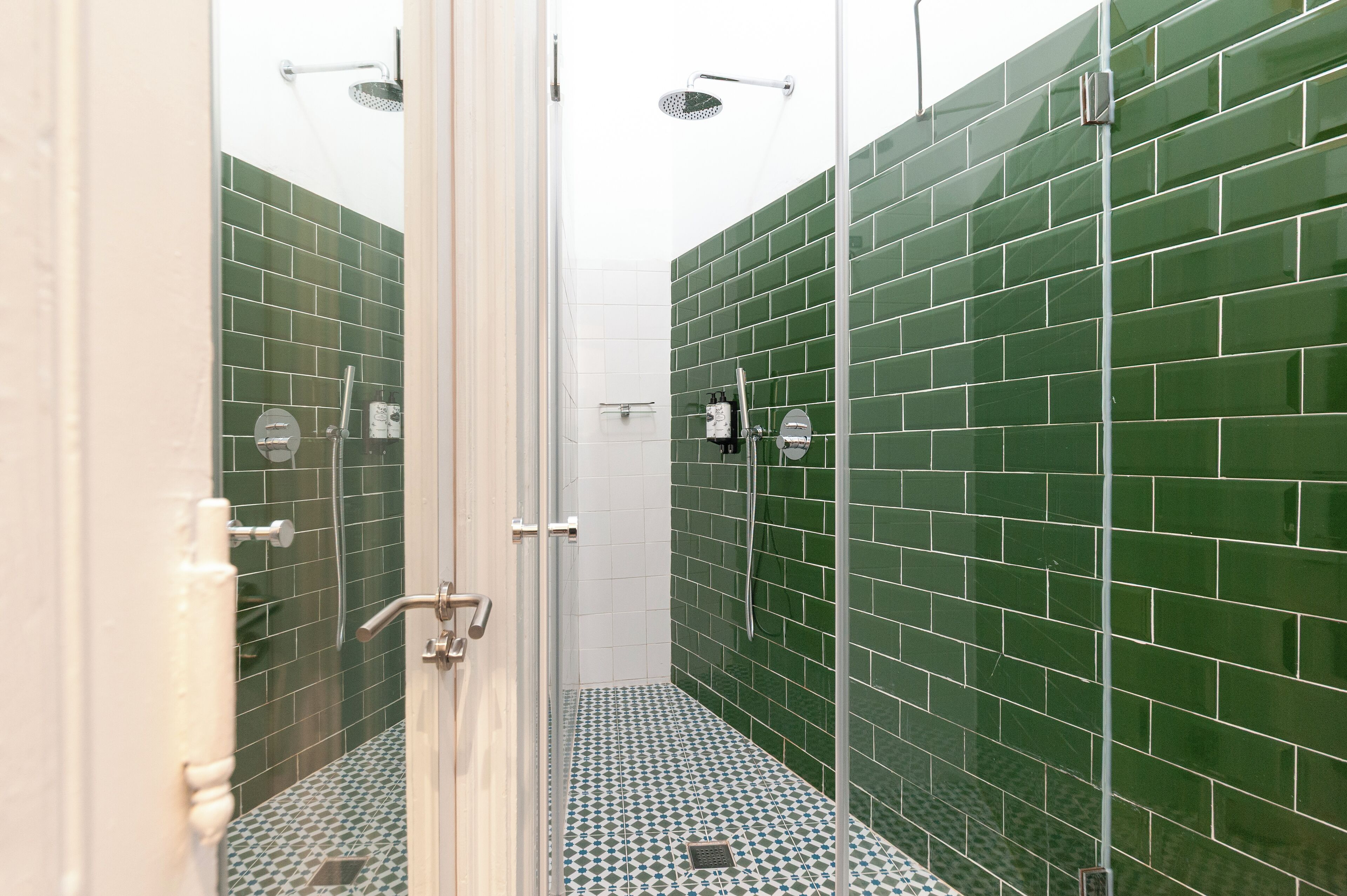 A modern bathroom with green tiled walls, a glass shower enclosure, and a patterned floor.