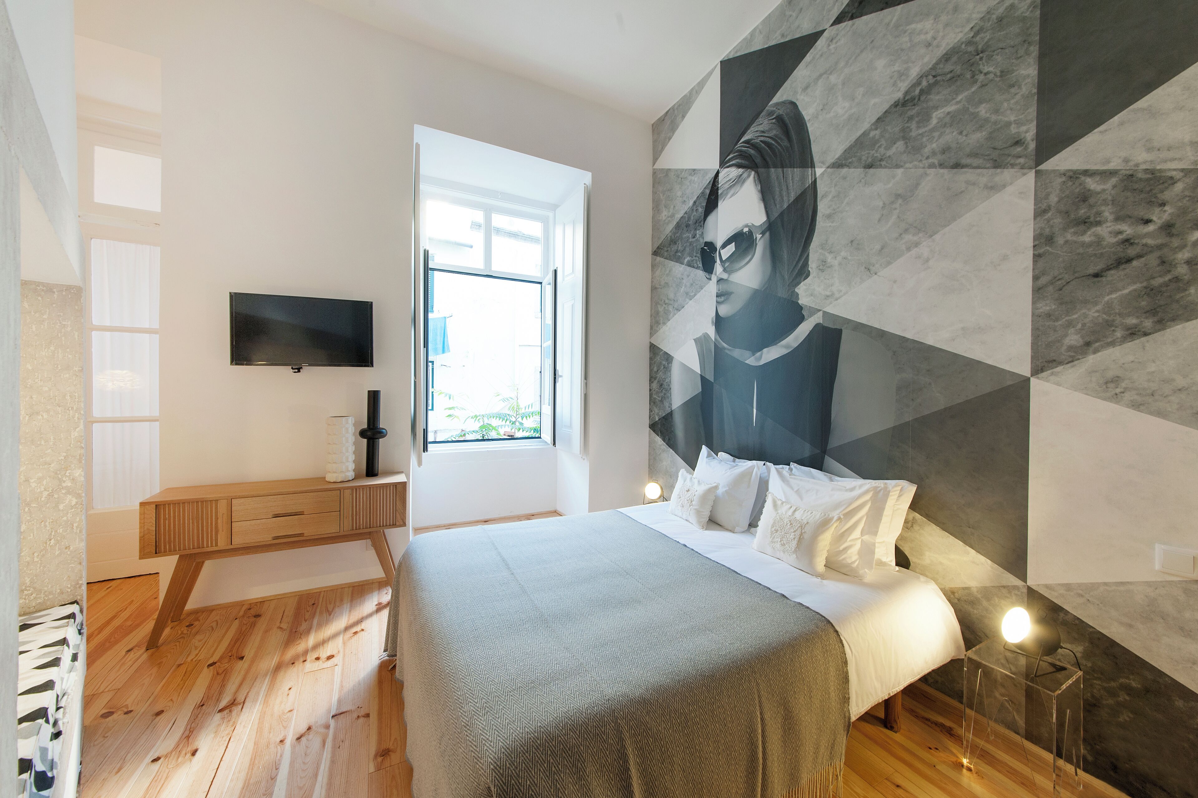 A modern bedroom with a bed, a desk, a TV, and a large geometric wall mural.
