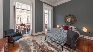 Un dormitorio moderno con un ventanal grande, un sofá, una cama y un espejo decorativo.