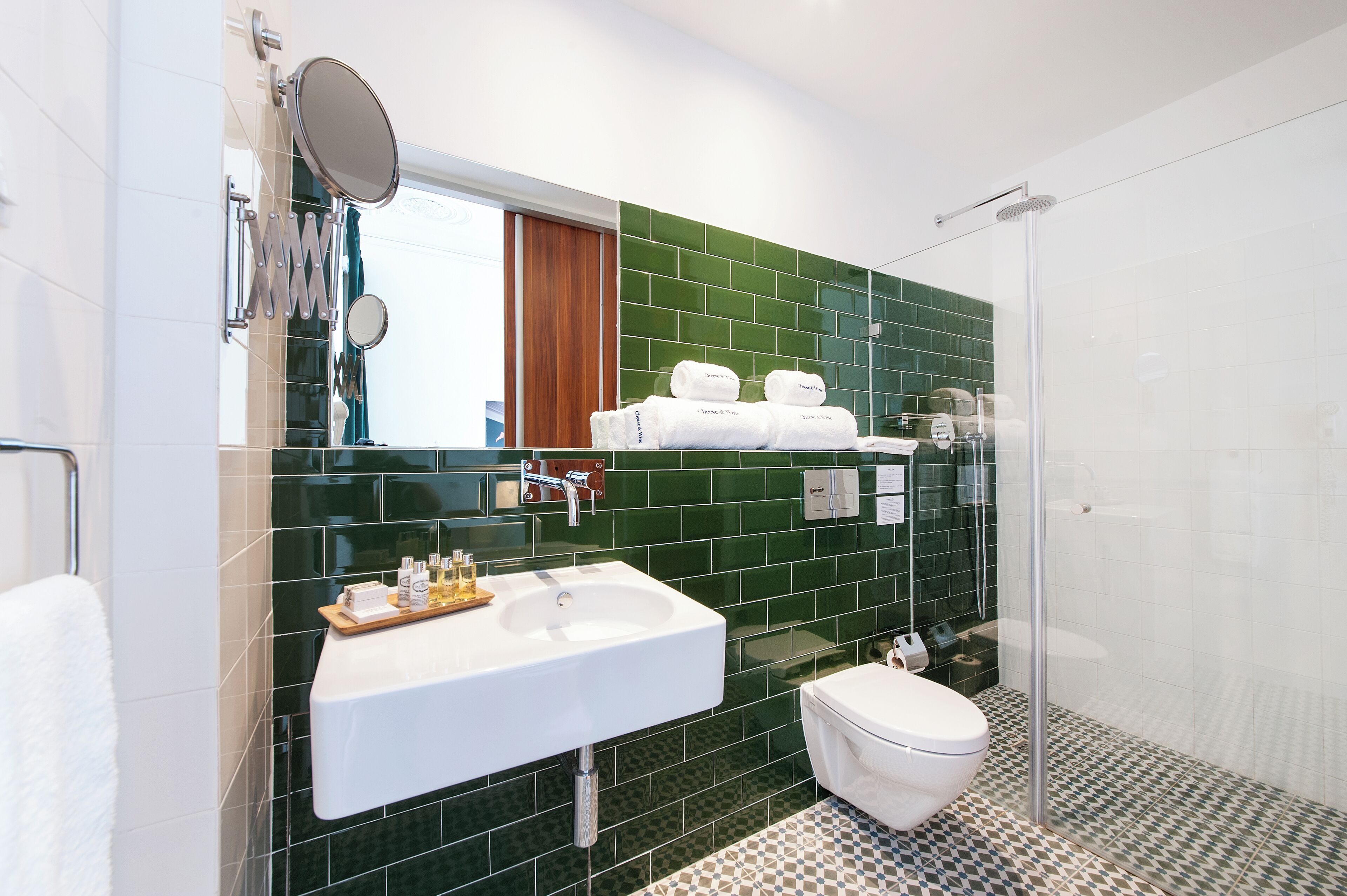 A modern bathroom with a white sink, green tiled walls, a glass shower enclosure, and a white toilet.