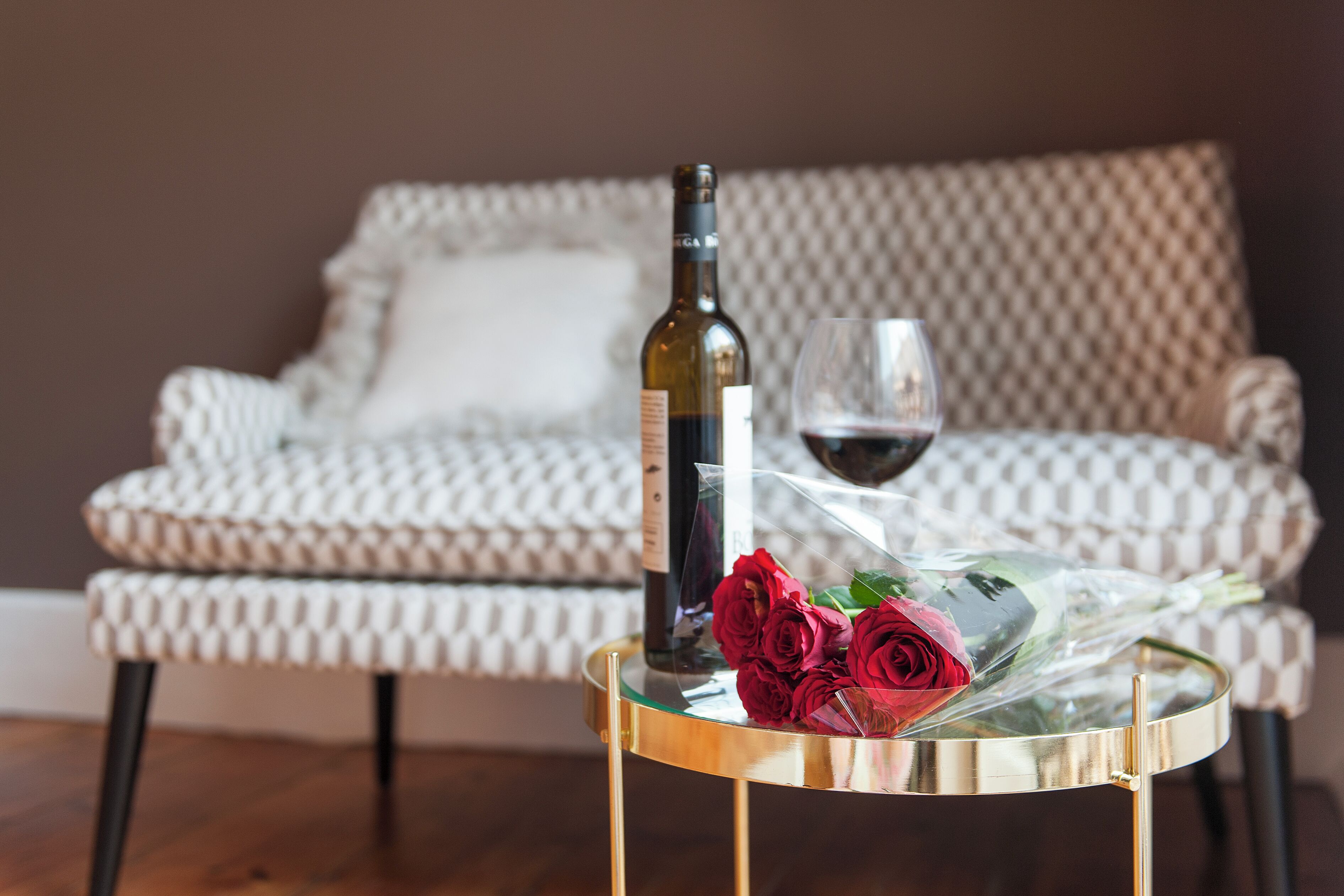A round glass table with a bottle and a glass of red wine, and a bouquet of red roses.