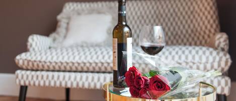 A round glass table with a bottle and a glass of red wine, and a bouquet of red roses.