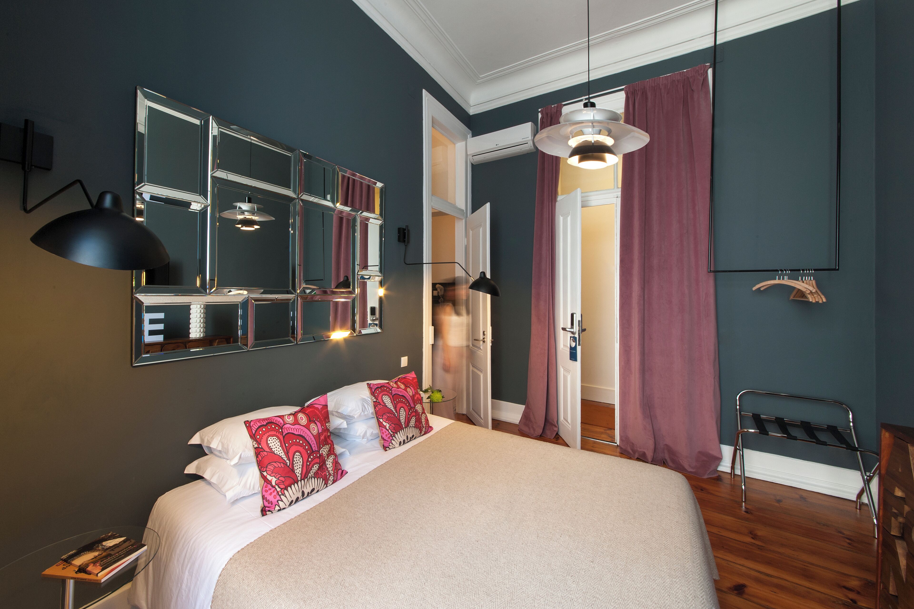Une chambre à coucher avec un grand lit, un miroir, une lampe suspendue et une porte donnant sur une autre pièce.