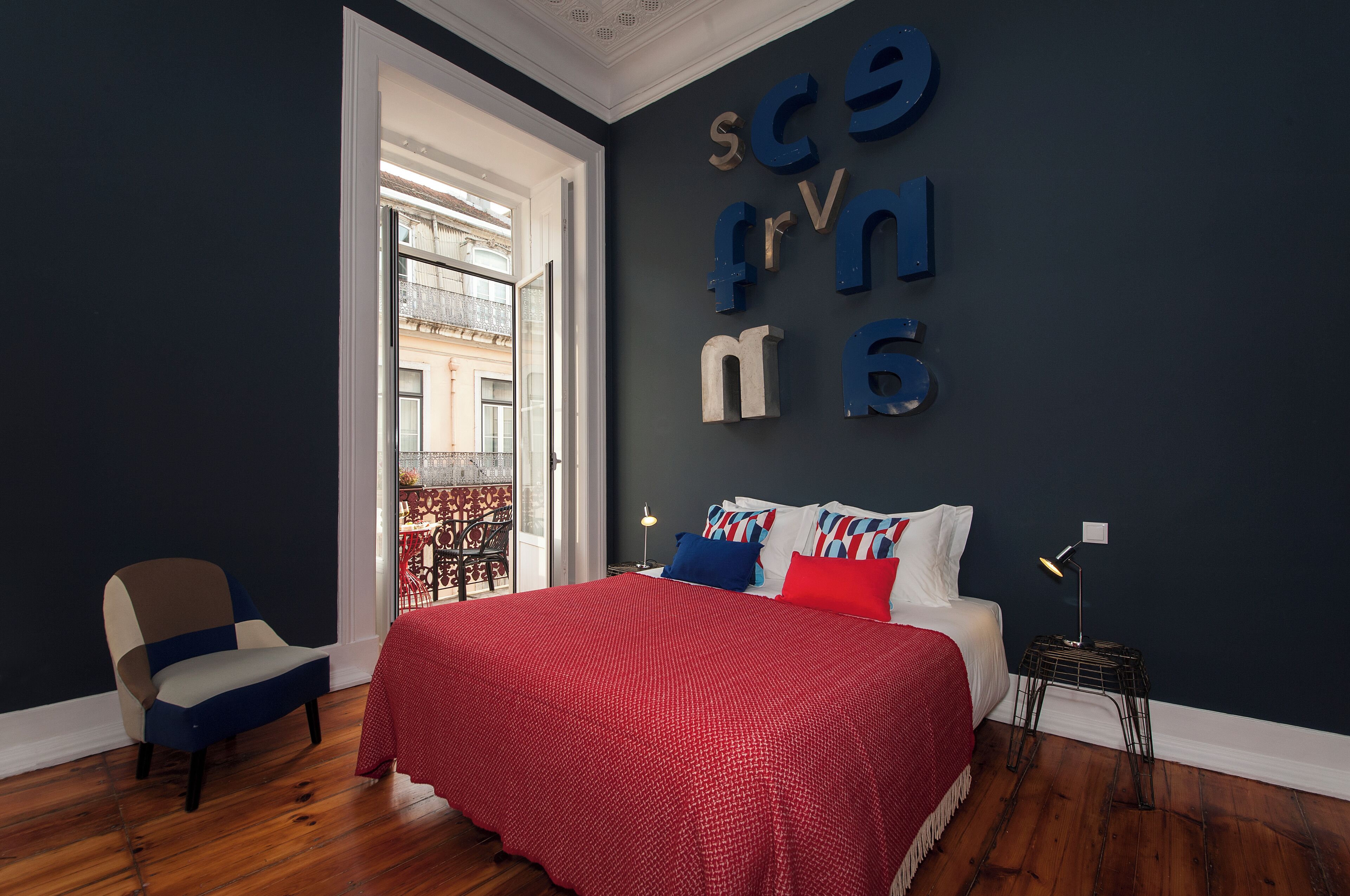 A bedroom with a bed, a chair, a nightstand, and a wall with letters spelling out a name.