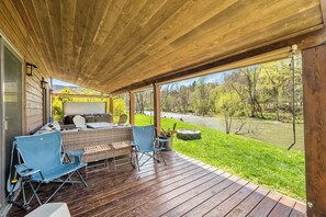 A covered deck with outdoor furniture, a grill, and a view of a river and forest. - Riverside retreat with hot tub, scenic views, rustic charm & open-plan luxury – perfect escape! (Pearisburg)