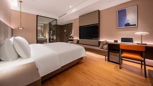 Una habitación de hotel moderna con una cama grande, un escritorio con una computadora portátil, un televisor y un espejo.