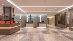 Un moderno vestíbulo de hotel con un mostrador de recepción, plantas en macetas y un mostrador de check-in.