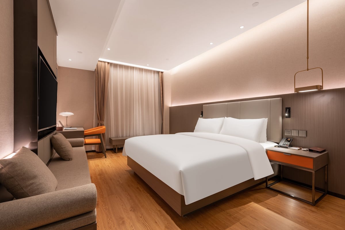 A modern hotel room with a large bed, a desk, a chair, and a television.