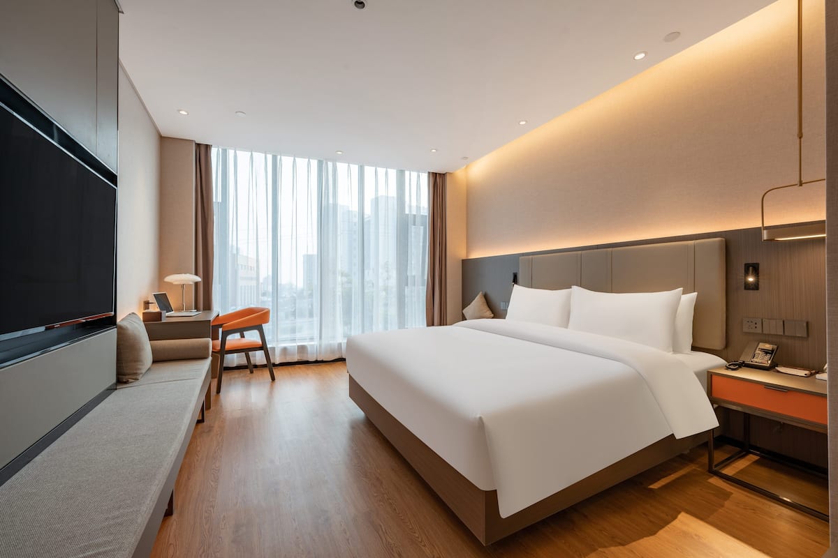 A modern hotel room with a large bed, a desk, a chair, and a TV.