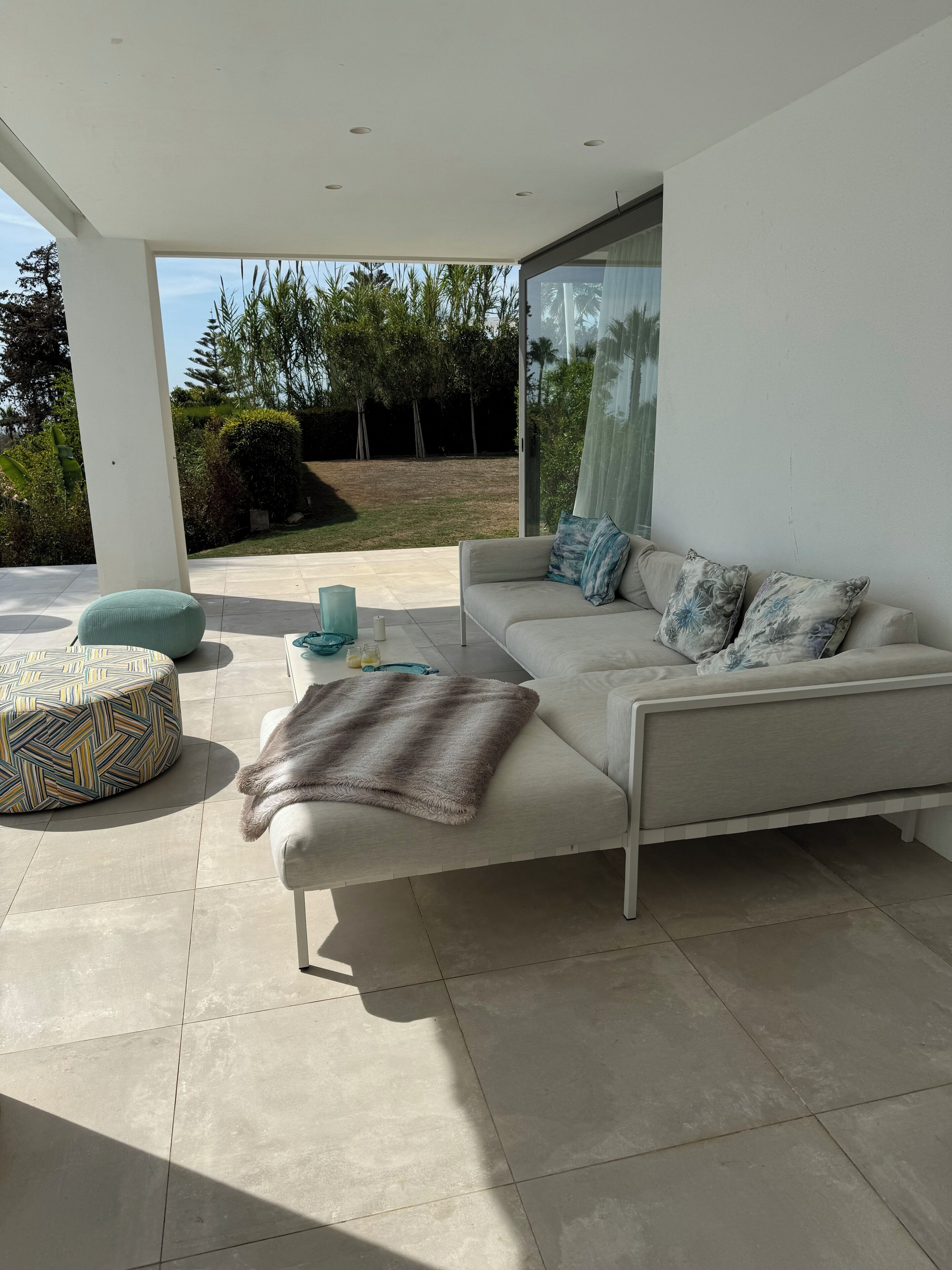 Una sala moderna con sofá, reposapiés y puerta de vidrio que da a un jardín.
