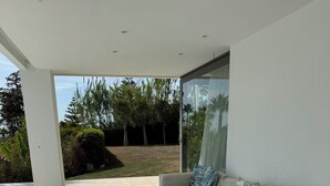 Un salon moderne avec un canapé, un pouf et une porte vitrée donnant sur un jardin.