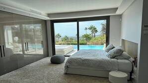 Une chambre à coucher moderne avec un grand lit, un petit pouf et une vue sur une piscine.