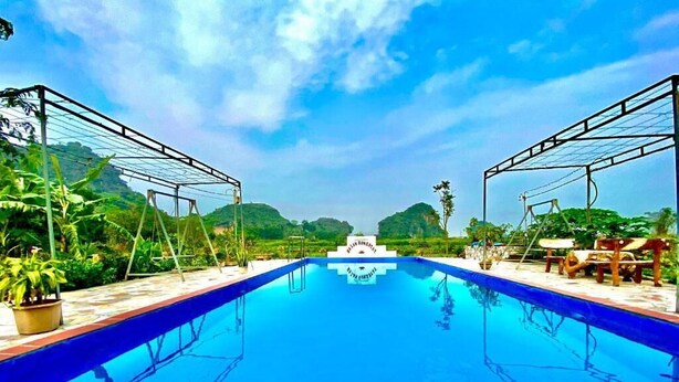 A swimming pool with a clear blue water surface, surrounded by lush greenery and a clear sky. - Ha Lan Homestay (Ninh Binh)
