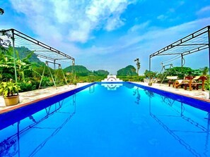 Ein Swimmingpool mit glasklar blauem Wasser, umgeben von üppiger Vegetation und wolkenlosem Himmel.