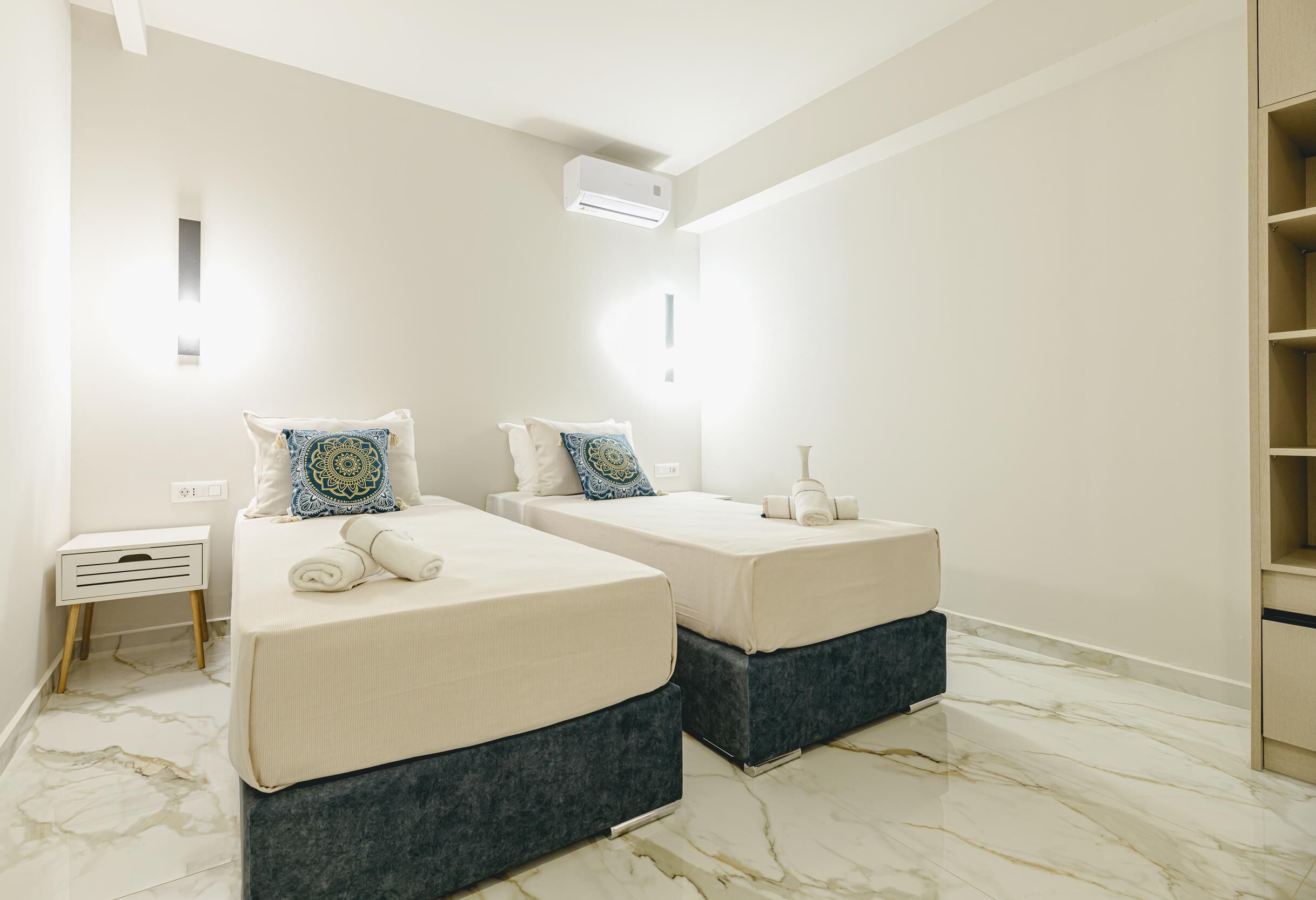 A modern bedroom with two beds, marble flooring, and a built-in wardrobe.
