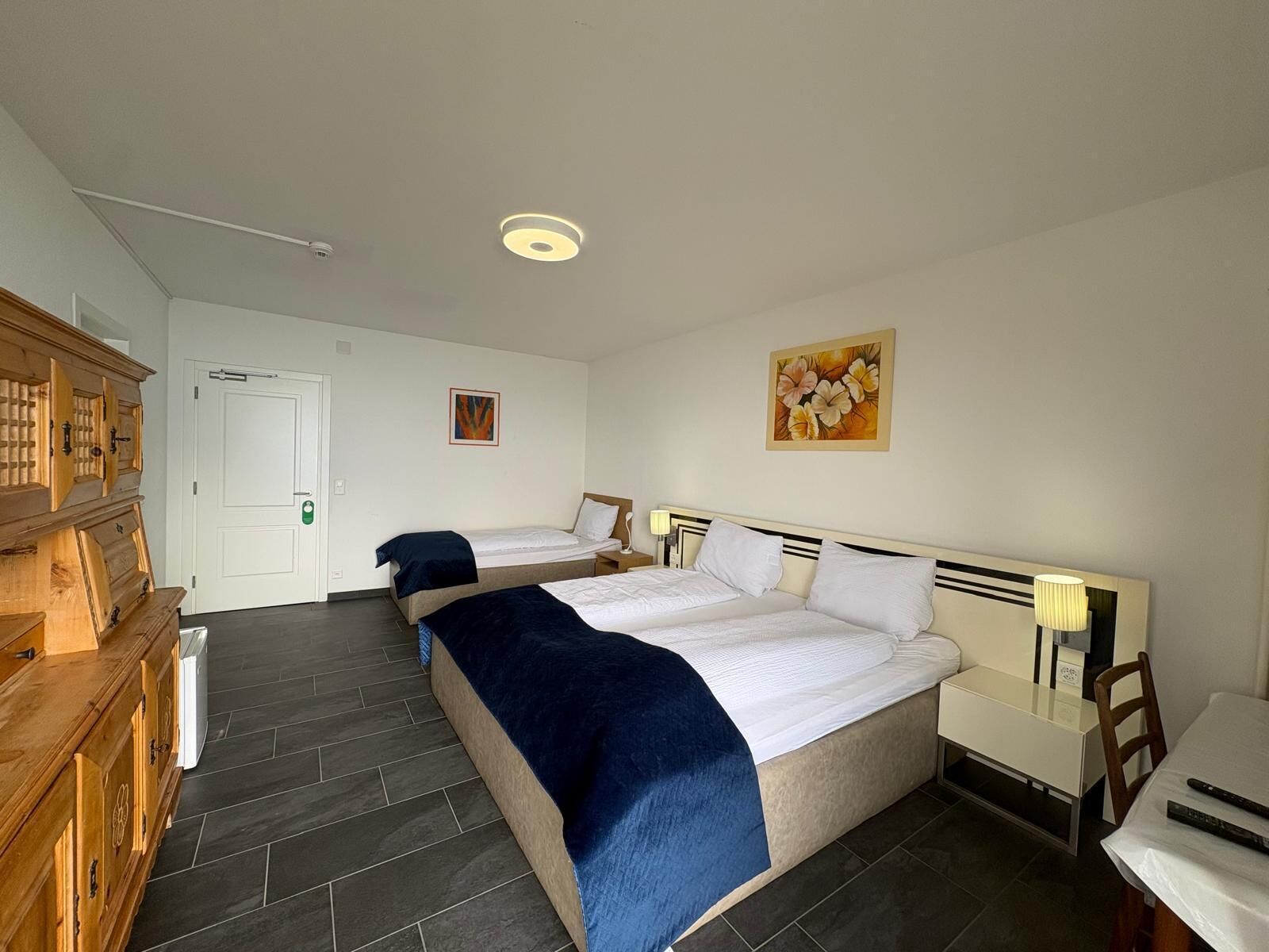 Une chambre d’hôtel avec deux lits, une armoire en bois, un tableau et un bureau avec une chaise.
