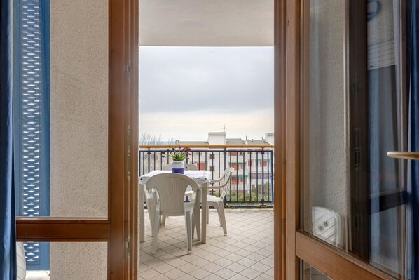 A balcony with a table and chairs, a potted plant, and a view of buildings in the distance.