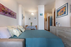 A bedroom with a bed, a dresser, a table with chairs, and artwork on the walls.