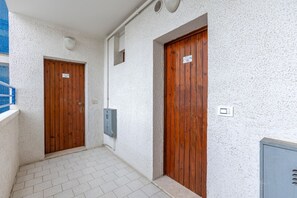 Deux portes en bois, chacune avec une plaque, un luminaire et un coffret électrique, le tout sur un mur blanc à la texture marquée.