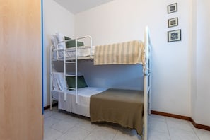 Une chambre avec des lits superposés, une porte en bois, des murs blancs et trois tableaux encadrés accrochés au mur.