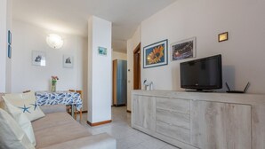 A living room with a sofa, a TV, a cabinet, and a dining area with a table and chairs. - GuestHost - Comfortable Apartment with Sea View (Lido delle Nazioni)