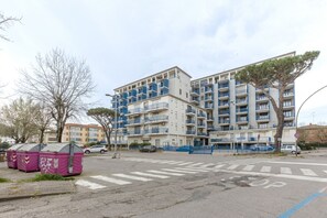 A multi-story residential building with balconies, a crosswalk, and parked cars.