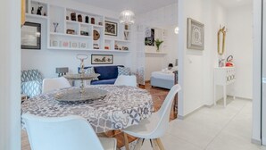 Un salon moderne comprenant un coin repas, des murs blancs et des étagères ornées de divers objets décoratifs.