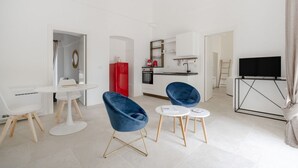A modern living room with a dining table, two blue chairs, a TV, and a kitchen area. - GuestHost Borgo Lucia with pool - Trullo Catenella (Selva di Fasano)