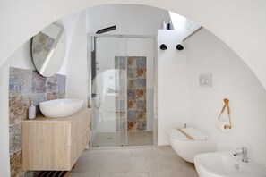 A modern bathroom with a freestanding sink, a glass-enclosed shower, a toilet, and a bidet.