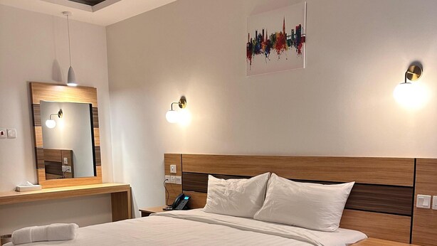 A modern hotel room with a large bed, bedside tables, a desk, and a chair. - 4 Guys Hotels (Muscat)