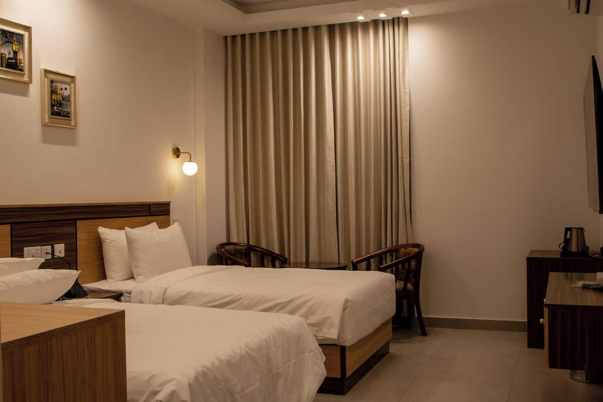 A hotel room with two beds, a wooden headboard, a desk with a kettle, and a curtain.