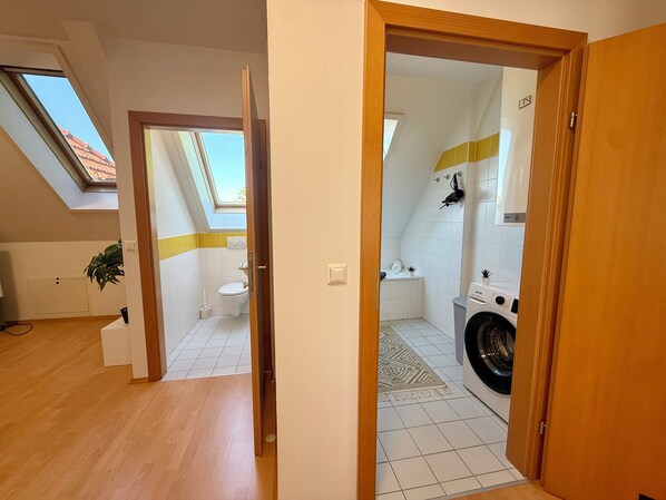 Una habitación con tragaluz, inodoro, lavadora y una pequeña planta.