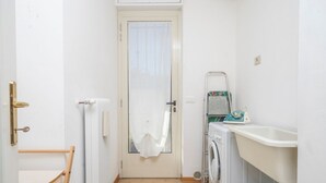 A compact laundry area with a washing machine, a drying rack, and a radiator. - GuestHost - Relax & Spacious Apartment X6 (Udine)