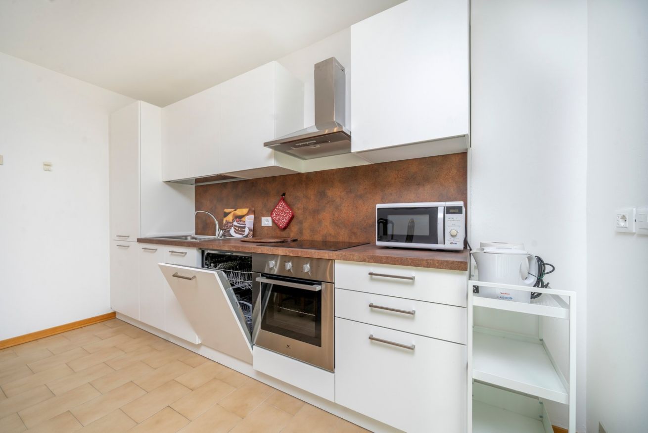 A modern kitchen with white cabinets, a stainless steel oven, a microwave, and a dish rack.