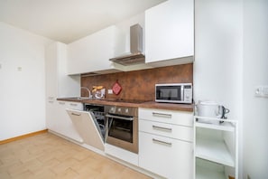A modern kitchen with white cabinets, a stainless steel oven, a microwave, and a dish rack.