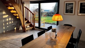 Un comedor con una mesa de madera, sillas, un florero de vidrio y una escalera que lleva a un balcón.
