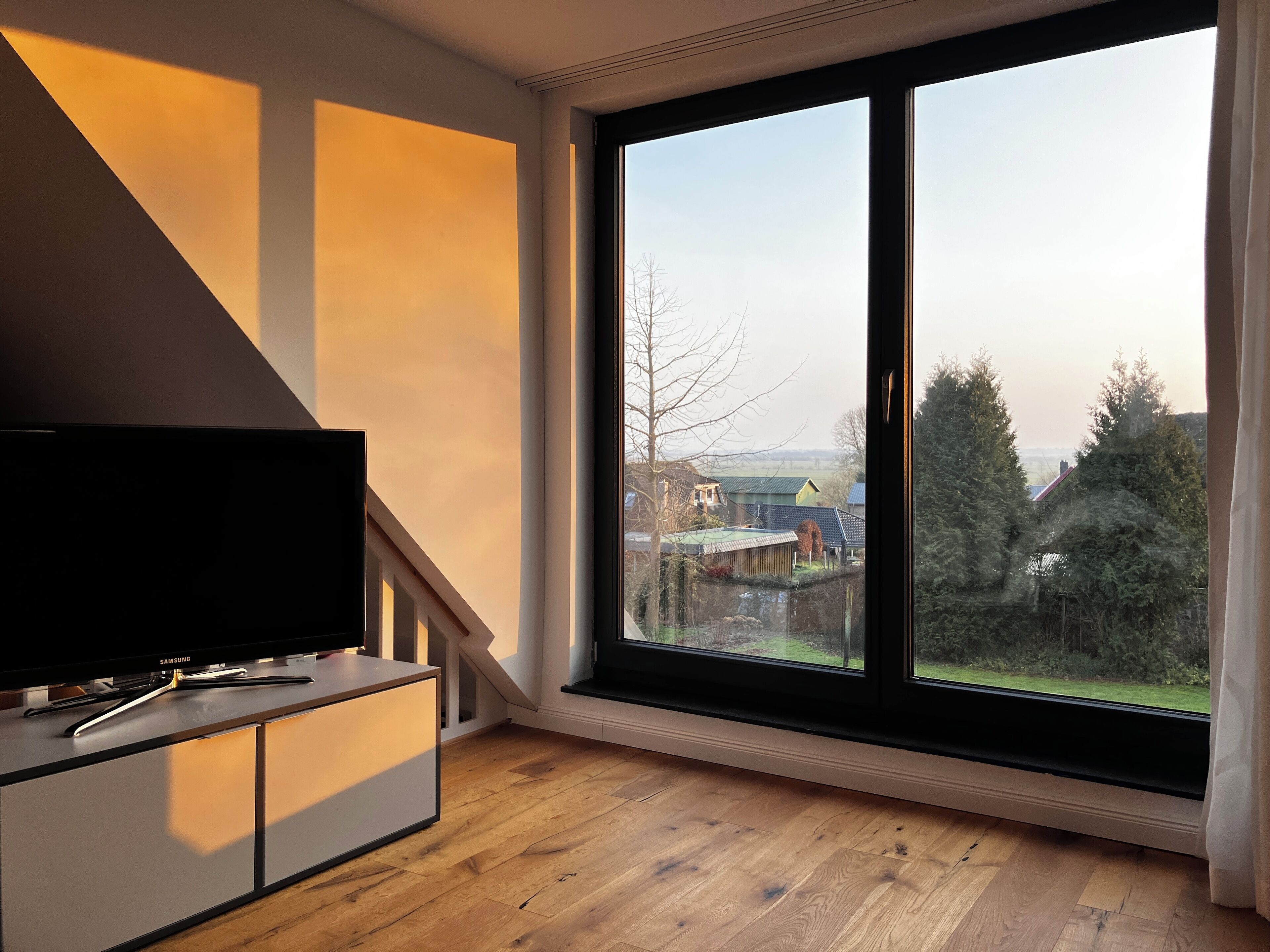 Un salon moderne avec une grande fenêtre, un téléviseur à écran plat et un plancher en bois.