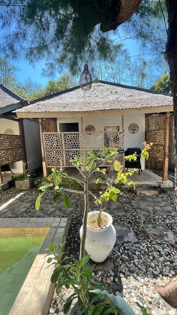 Une cour avec un petit arbre planté dans un pot, une terrasse carrelée et un bâtiment doté d’un toit en tuiles et de murs en bois.