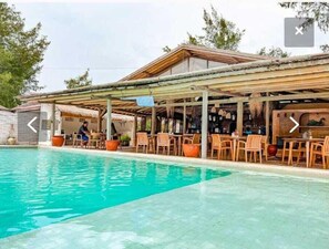 Een zwembadgedeelte met een overdekte zithoek, een bar en een bord waarop 'Grill' staat.
