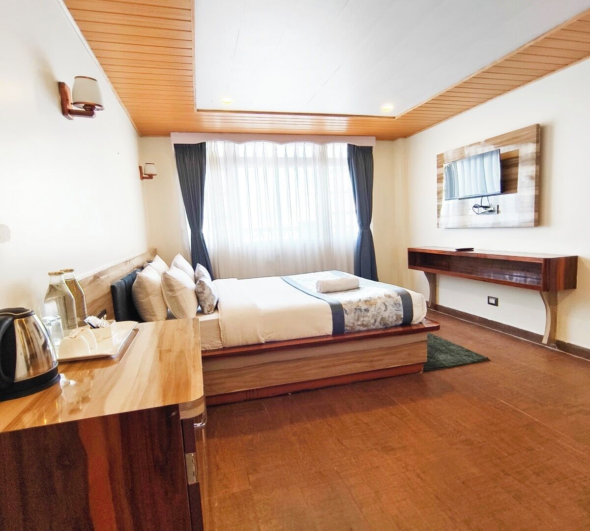 Habitación de hotel con cama de madera, escritorio con hervidor y espejo en la pared.