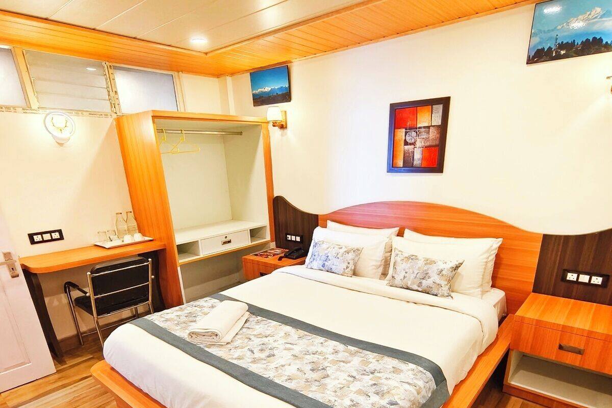 Camera d'albergo con un letto grande, testiera in legno, una scrivania con sedia, uno specchio e un comodino con lampada.
