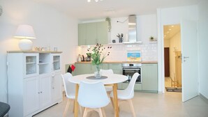Une cuisine moderne avec des meubles blancs, une table à manger entourée de chaises blanches et un petit îlot central agrémenté d’une lampe.