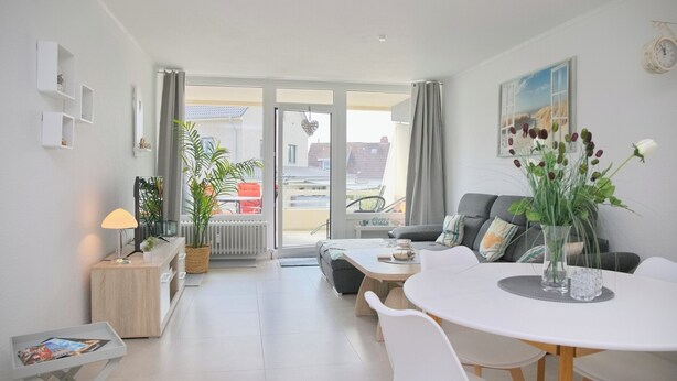 Un salon moderne avec un canapé blanc, une table à manger avec des chaises, une table basse et une plante en pot.
