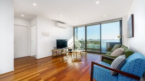 Un vaste espace de vie comprenant une grande porte-fenêtre coulissante donnant sur un balcon, un téléviseur et un coin salon avec un canapé à motifs.