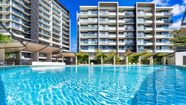 Une piscine à l’eau d’un bleu cristallin, entourée d’immeubles d’appartements modernes dotés de balcons.