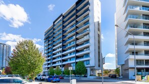 Un immeuble résidentiel à plusieurs étages, doté de balcons, d’un parking et surplombant un ciel dégagé.