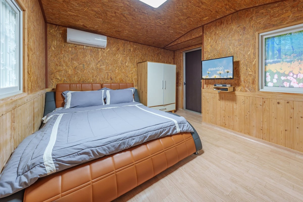 Quarto com cama, guarda-roupa, televisão e janela com uma pintura.