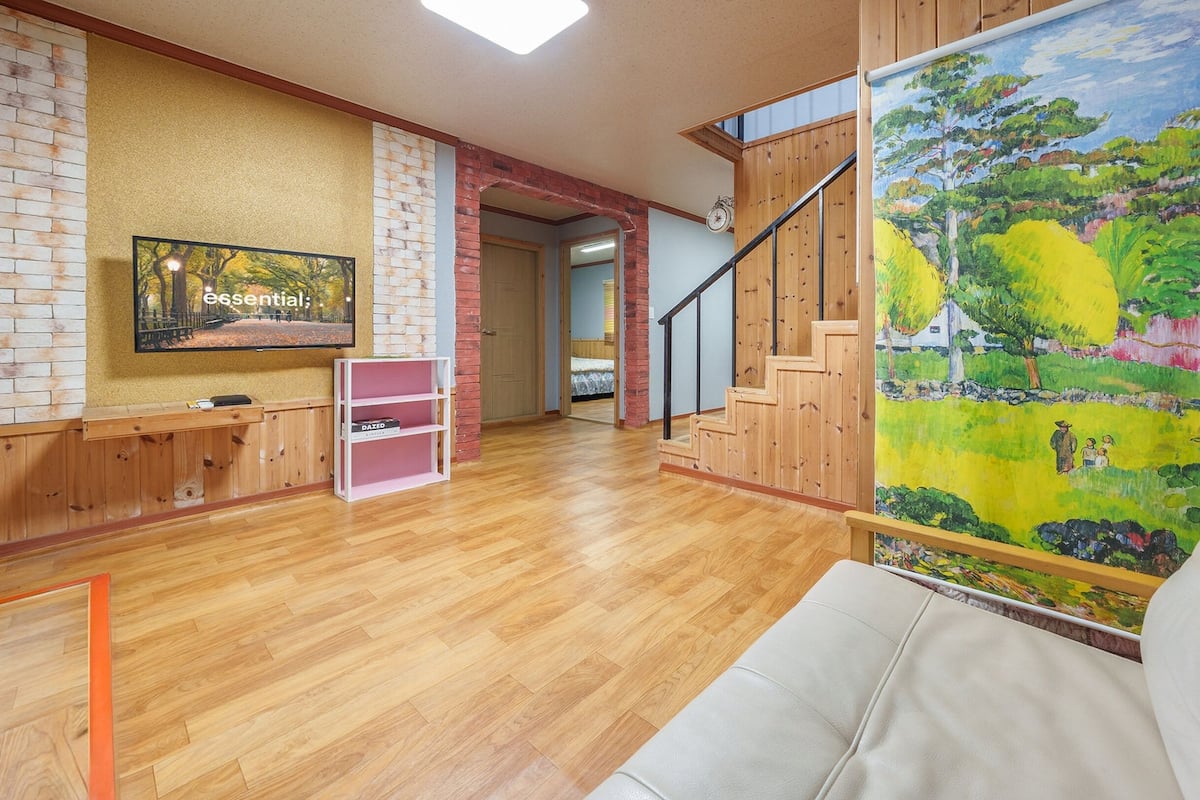 Uma sala de estar ampla com piso de madeira, um sofá branco, um quadro e uma escada.